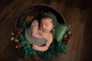 baby boy wrapped in a green swaddle and in a wooden bowl fast asleep
