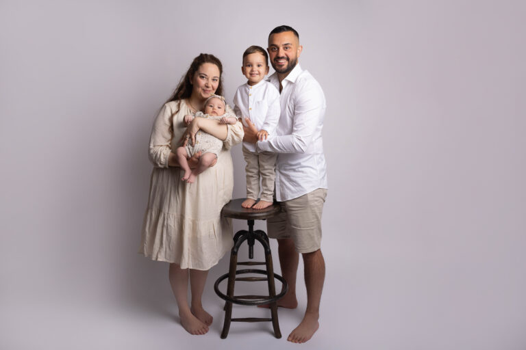 family of man, woman, little boy and baby in arms, in front of a beige wall by Newborn and family Photographer in Hull