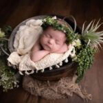 baby girl asleep in a bucket with a beige blanket and a green hairband by Hull newborn photographer
