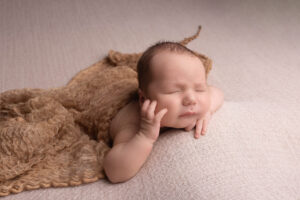 baby lying on their tummy with hand on cheek, on a beige blanket by Newborn Photographer in Hull