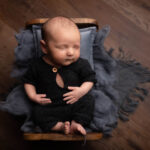 baby boy in a blue romper asleep on a wooden bed by Hull newborn photographer