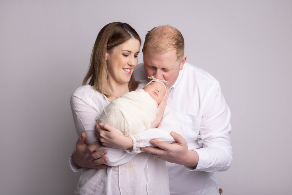 mum and dad wearing white with baby on a beige background by Hull newborn photographer