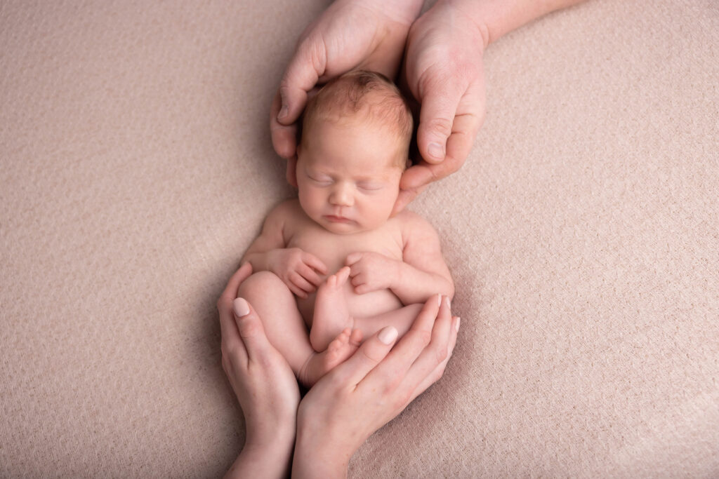 baby asleep in mym and dad's hands on a cream blanket by Hull newborn photographer