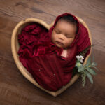 baby girl wrapped in deep red and in a heart shaped wooden bowl by Hull newborn photographer