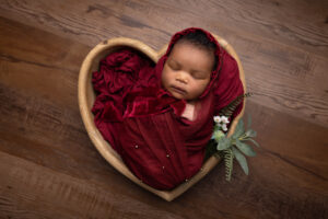 baby girl wrapped in deep red and in a heart shaped wooden bowl by Hull newborn photographer