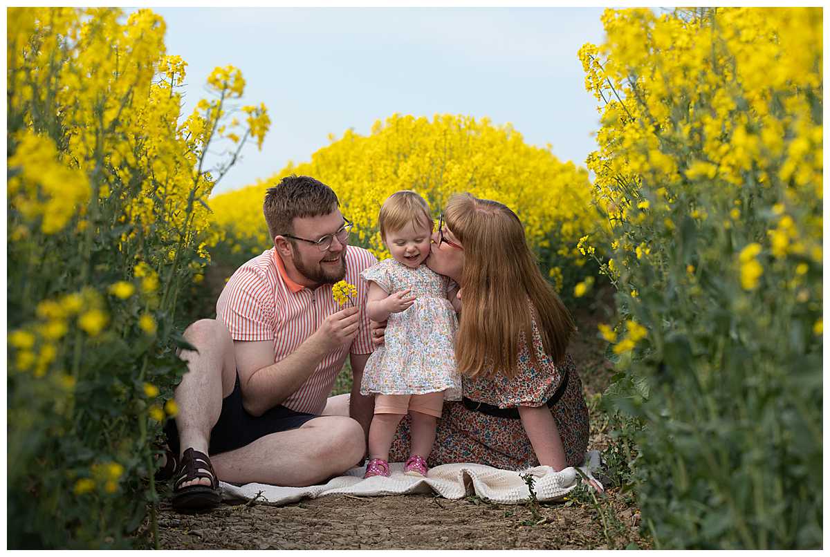 parents with a toddler in a field of yellow flowers by family photographer in Hull